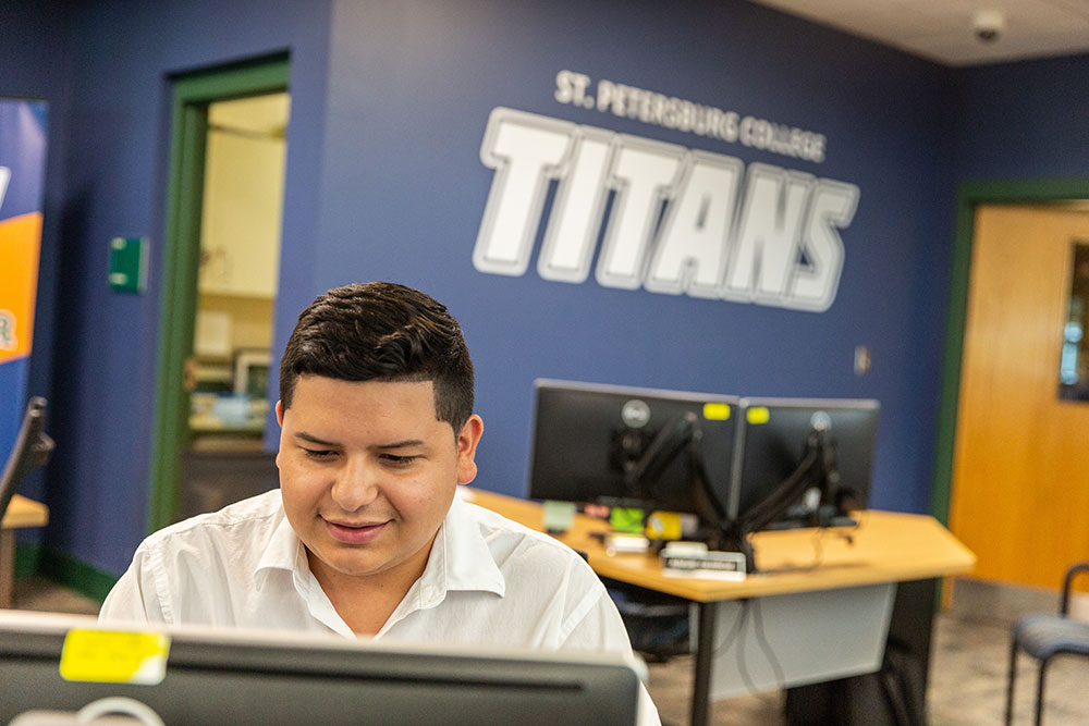 male student sitting at a computer in front of wall with Titans logo