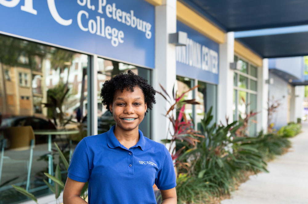 female SPC student wearing a blue polo short standing in front of the Downtown Center