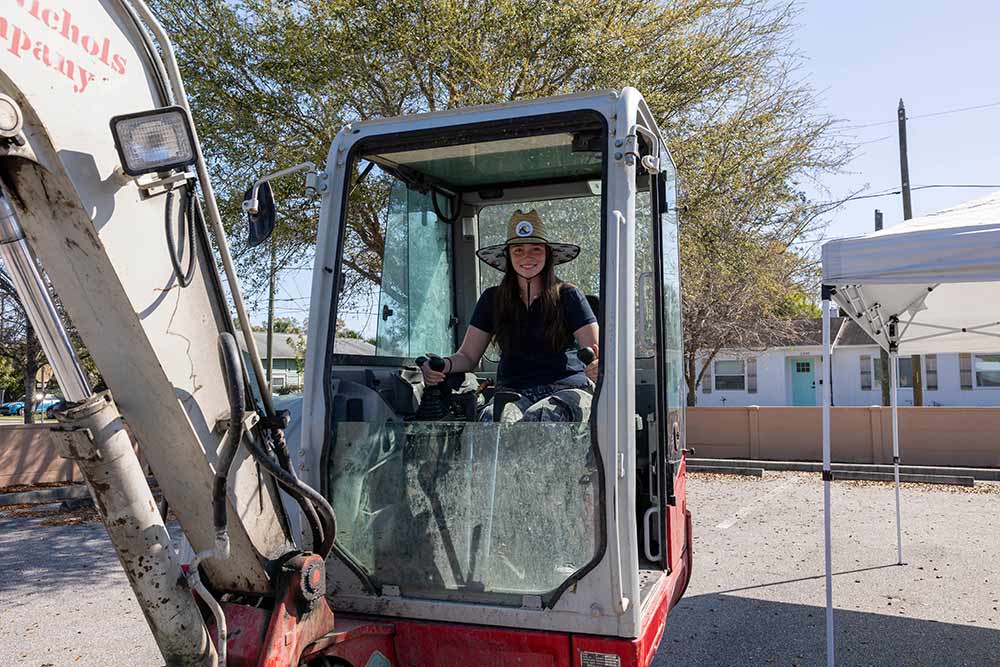 female student wearing a sumbrero driving a bulldozer