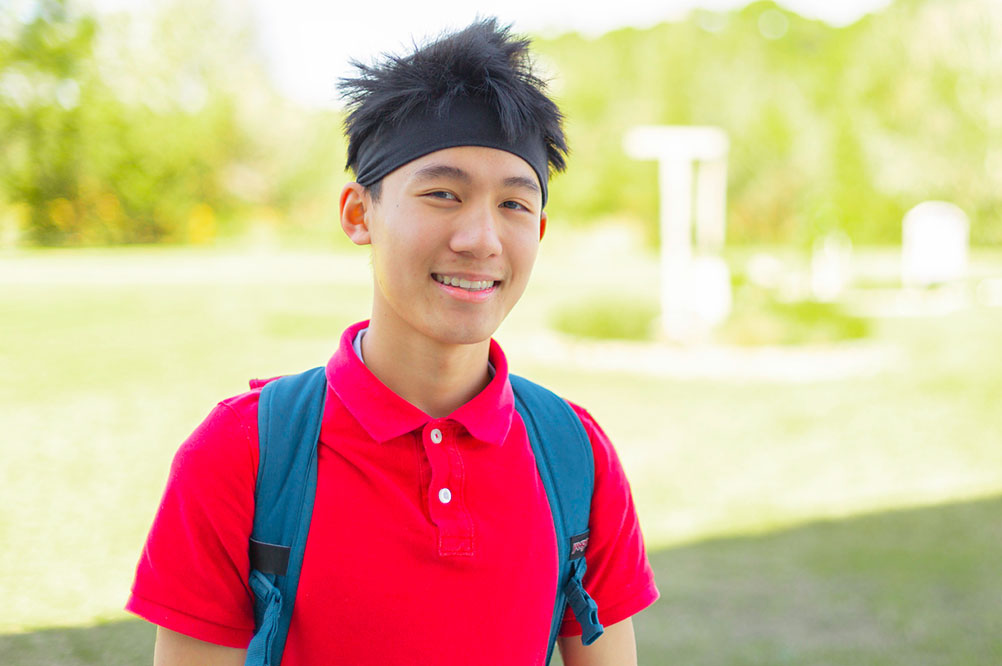 male student wearing a red polo shirt, black headband and a blue background