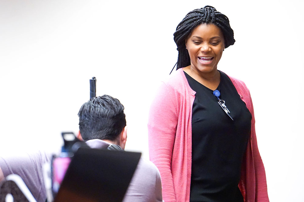 female SPC employee wearing a pink jacket smiling whilst talking to someone sitting down