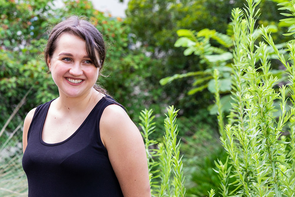 female student smiling wearing a black tank top in front of a tree