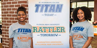 2 IGNITE program students posing in front of a poster 