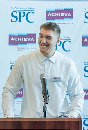 student Eno Mucaj smiling while speaking at a podium
