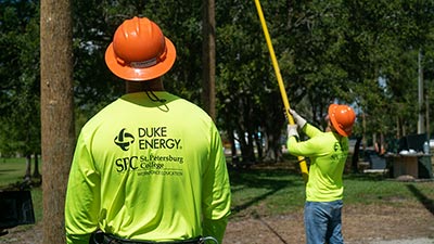 a lineworker training at SPC wearing a neon yellow shirt and orange helmet observing another lineworker also in a yellow shirt and orange helmet