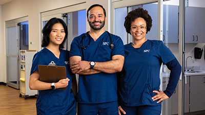 female, male and female nursing students wearing blue scurbs with their arms folded