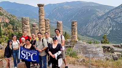 a group of students on a study abroad trip to greece carrying a blue SPC flag