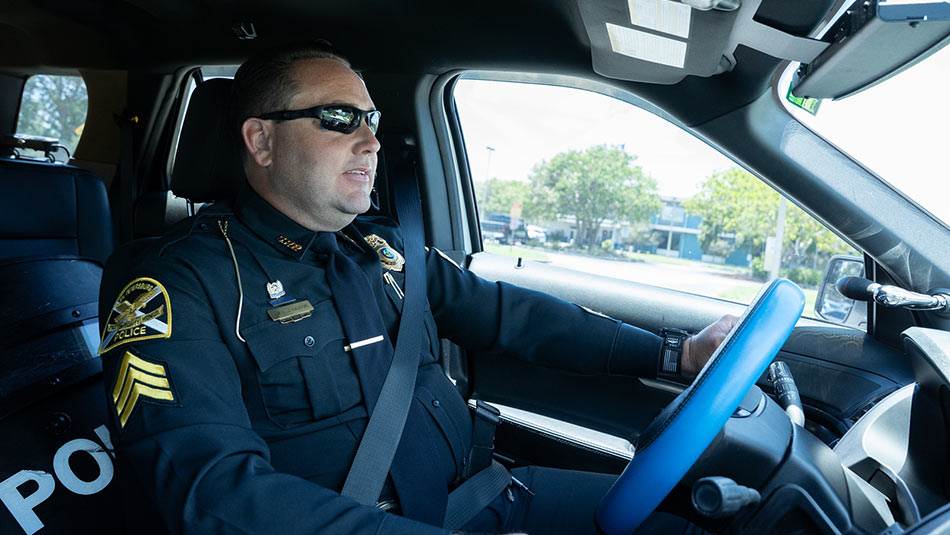 male police officer wearing a blue uniform sitting in the front seat of his patrol car