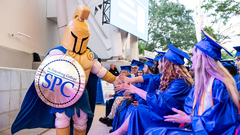 Titus the Titan mascot gives a group of graduates high fives during Spring 2025 graduation ceremony