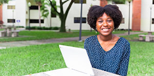 student sitting outside, on campus with her laptop, smiling