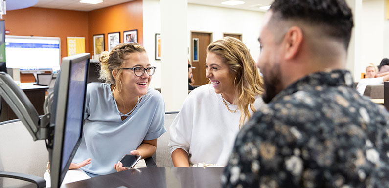 two young women and one young man interacting in front of a computer monitor