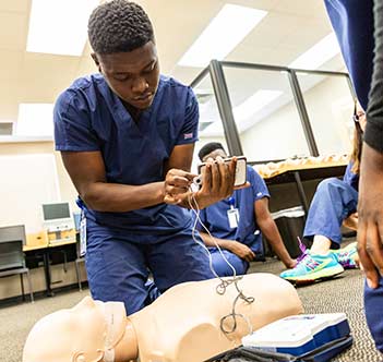young man in scrubs readying a dummy to practice CPR on