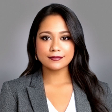 A portrait of Sarah Deonarinesingh, wearing a gray blazer over a white shirt, in fornt of a gray background.