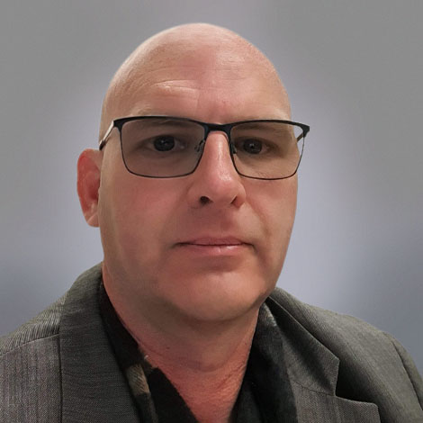 A portrait of Todd Irvine wearing a gray sport coat and dark-rimmed glasses.