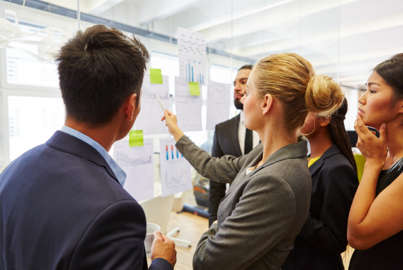 a group of people in a corporate setting, reviewing reports on a white board