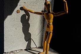 Student digital media project. Photograph of a wooden art mannequin striking a post next to a concrete wall.