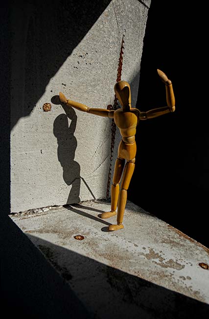 Student digital media project. Photograph of a wooden art mannequin striking a post next to a concrete wall.