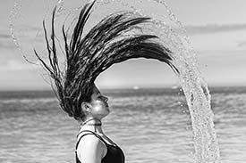 Student digital media project. Photograph of a woman flipping her soaking hair over her head. Water arches dramatically from her hair.