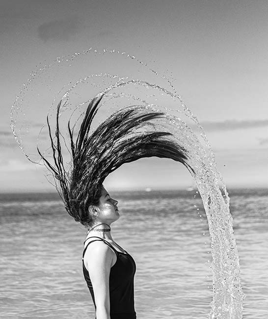 Student digital media project. Photograph of a woman flipping her soaking hair over her head. Water arches dramatically from her hair.