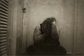 Student digital media project. Grainy black and white photograph of a woman sitting on the ground and holding her face in her hands.
