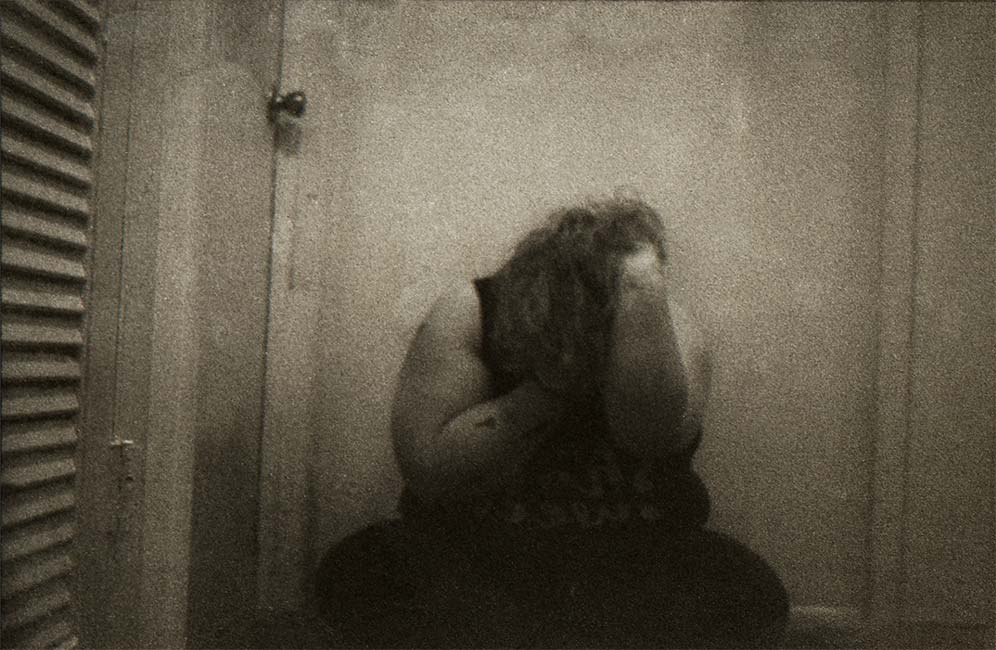 Student digital media project. Grainy black and white photograph of a woman sitting on the ground and holding her face in her hands.