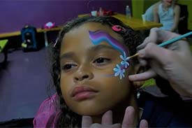 A child getting flowers and a rainbow painted on her face. A child getting flowers and a rainbow painted on her face.