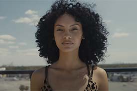 A woman with curly dark hair on a balcony with blue sky and the horizon behind her. A woman with curly dark hair on a balcony with blue sky and the horizon behind her.
