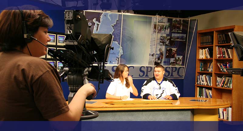 SPC Students sitting at a broadcast desk in a television studio in front of cameras