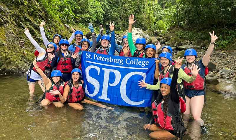 group of SPC students wearing helmets holding an SPC flag in a Costa Rican rainforest