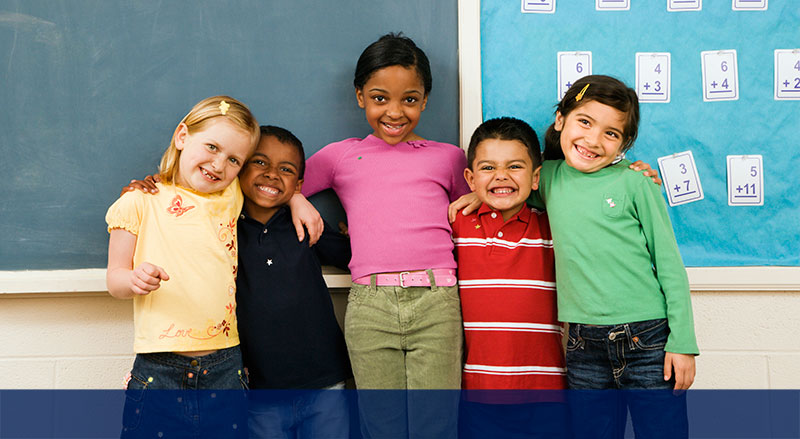 group of five preschool and elementary aged children smiling with their arms around each others' shoulders