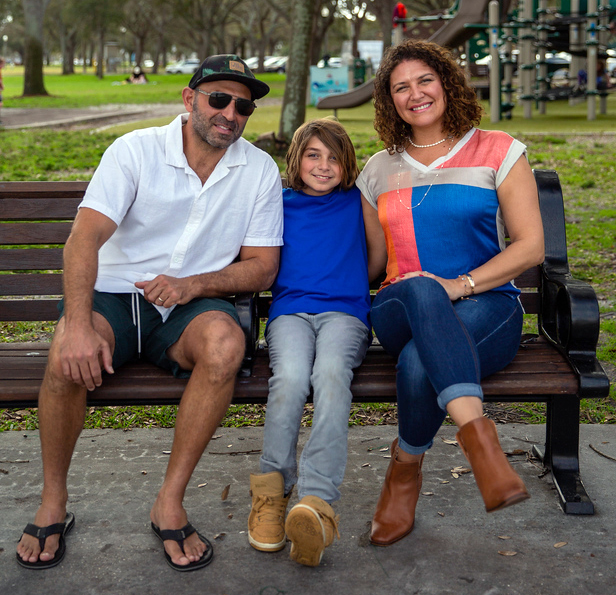Images/degrees-training/education/luisa-family-park.jpg Luisa Shamas sits on a park bench with her husband and son, a children's playground in the background