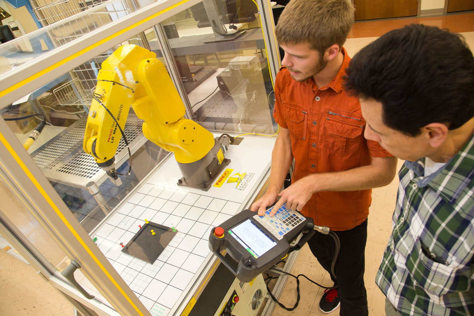 an instructor overseeing a student controlling a robotic arm