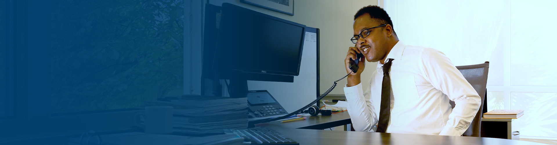 young man seated at a desk in front of a computer talking on the phone