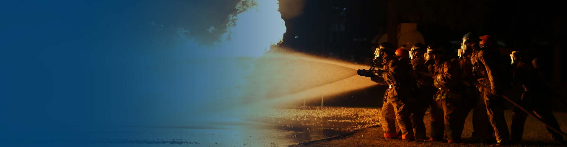 Fire fighters holding a high pressure water hose and dowsing an active fire