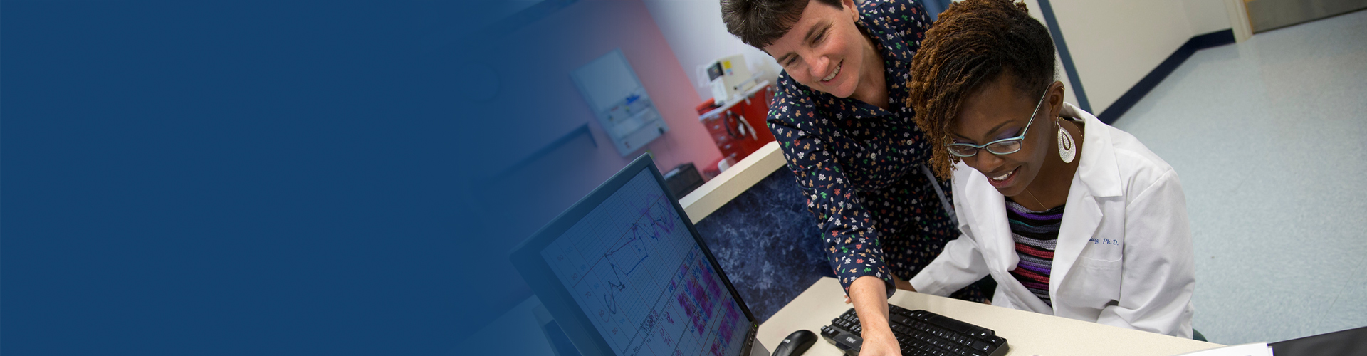 image of a faculty staff smiling with a student who is seated in front of a computer