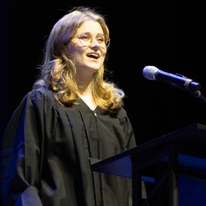 photo of Elizabeth Daley wearing a graduation gown standing in front of a microphone