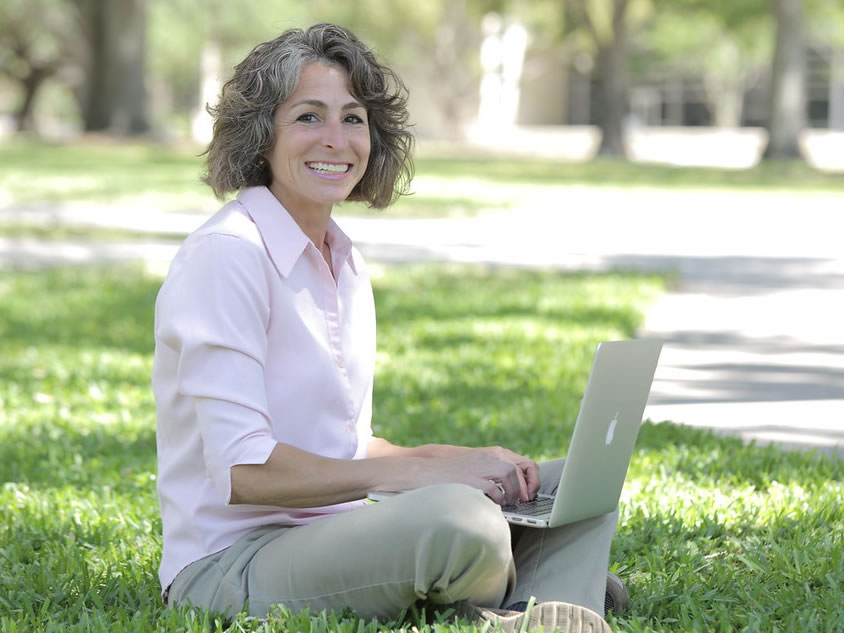 Desiree Solito seated outdoors with her laptop smiling at the camera