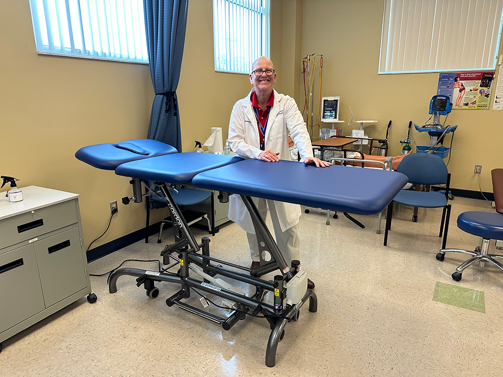 physcial therapy assistant instructor smiling in back of the new physical therapy table