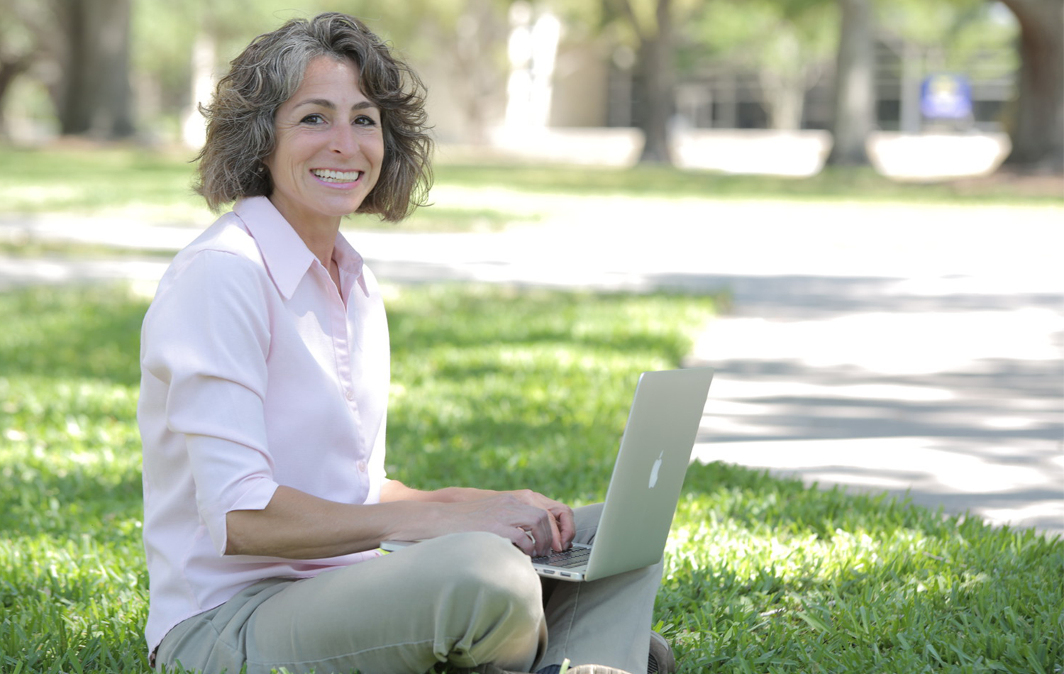 a woman on campus, sitting in the grass, using a laptop