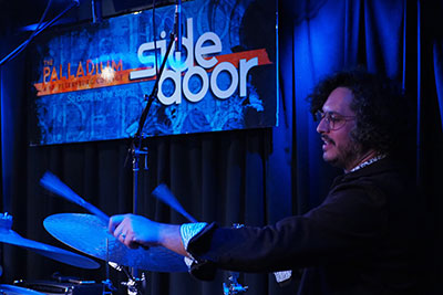A drummer playing at a Palladium event under blue lights