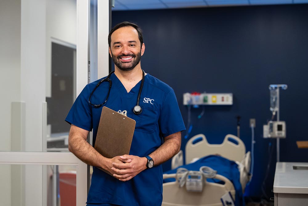 male nursing student in blue scrubs holding a clip board