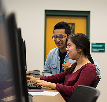 two students talking in front of computer monitors