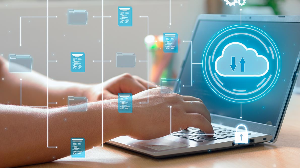 transparent icons of files superimposed on a laptop with a cloud on it and two hands on the keyboard