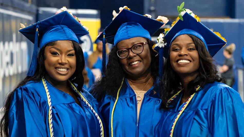 Three female SPC graduates wearing their caps and gowns smiling at their graduation ceremony