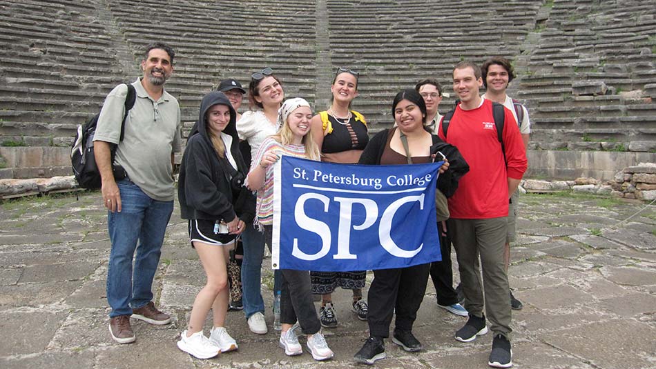 A group of students hold an SPC sign in front of a beautiful backdrop of the Greek landscape.