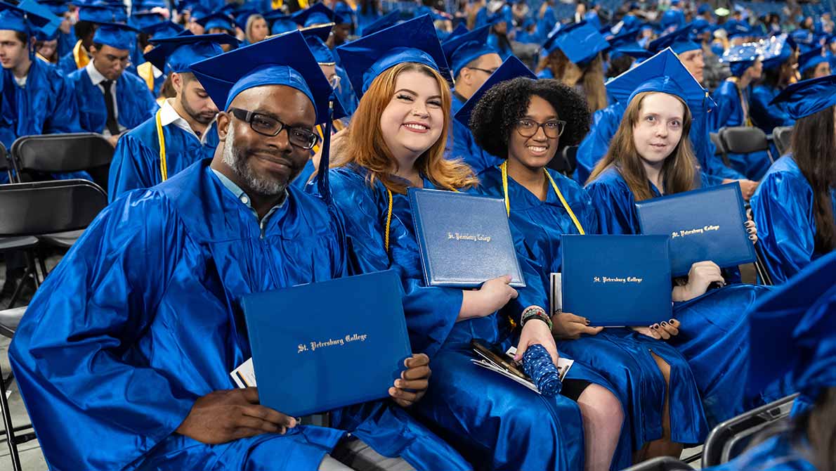 four SPC graduates holding their diplomas during commencement ceremony