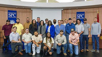 17 graduates of SPC's lineworker program pose with SPC President Dr. Tonjua Williams