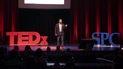 a male presenter on stage between 3-d models with the letters TEDx and SPC