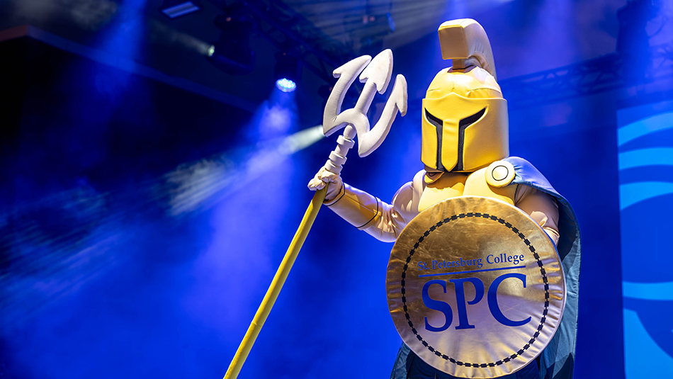 SPC Mascot Titus the Titan in his yellow costume and holding a spear congratulating 2024 graduates at commencment