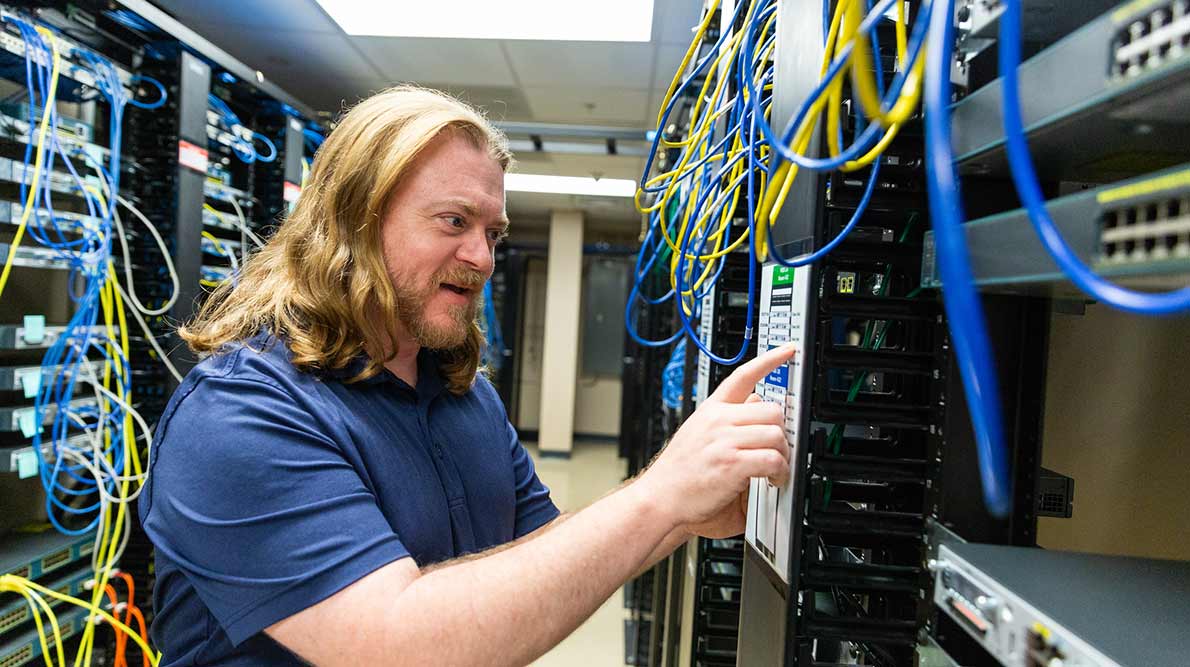 male student with long blond hair working in a room of computer servers